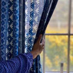 a person is opening the curtains in front of a window with blue and white patterns