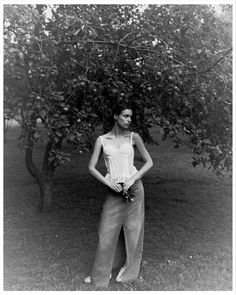 black and white photograph of a woman standing in front of an apple tree with her hands on her hips