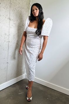 a woman standing in front of a wall wearing a white dress with an angel wings on it