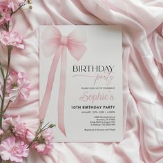 a birthday party card with pink flowers and ribbon on the front, surrounded by satin fabric