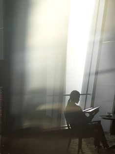 a person sitting on a bench in front of a window with the sun shining through