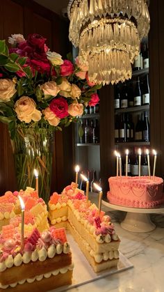 a table topped with cakes and candles next to a vase filled with flowers on top of a counter