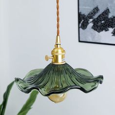 a green glass lamp hanging from a gold colored light fixture in a white room with a painting on the wall behind it