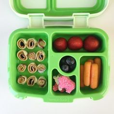 a green lunch box filled with fruits and veggies on top of a white table