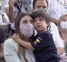 a woman holding a child wearing a face mask in front of a group of people