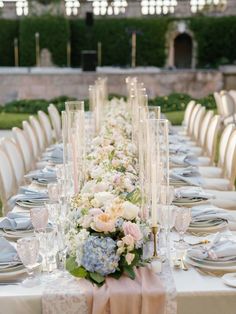 a long table is set with white and pink flowers, silverware, candles, and napkins