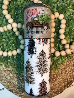 a white and black canister with pine trees on it next to some green plants