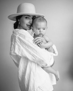 a woman holding a baby in her arms and wearing a hat on top of her head