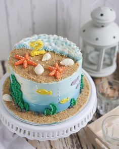 a decorated cake sitting on top of a white platter next to a candle and seashells