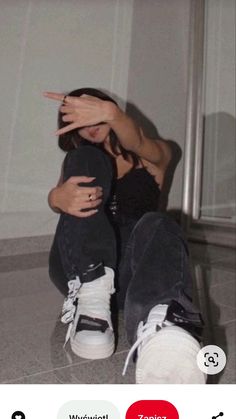 a woman sitting on the floor with her hand up to her face and two fingers in front of her face