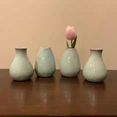 three vases sitting on top of a wooden table next to a pink tulip