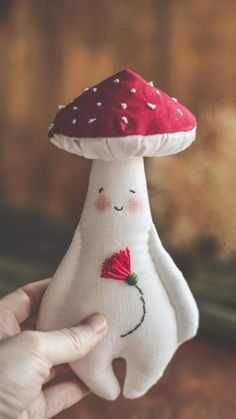 a hand holding a stuffed mushroom with a red flower on it's head and eyes