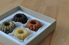 four different types of donuts in a box on a wooden table with one missing