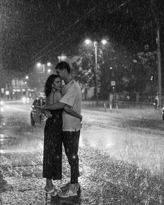 a man and woman standing in the rain under an umbrella at night with their arms around each other