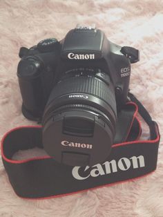 a canon camera sitting on top of a white carpet next to a black strap with the word canon written on it