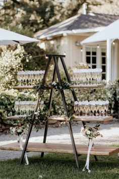 a wooden stand with wine glasses and flowers on it in front of a white house