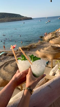 two people toasting on the beach with cocktails in their hands and umbrellas flying above them