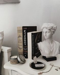 a white table topped with books and a busturine next to a candle holder