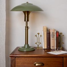 a green lamp sitting on top of a wooden table next to books and an open book