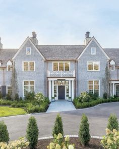 a large gray house with lots of windows and bushes in front of the entrance to it