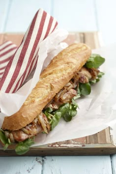 a sandwich with meat, lettuce and tomatoes on a cutting board next to a striped napkin