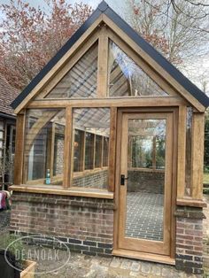 a small wooden greenhouse with glass doors and brick walkway leading up to the front door