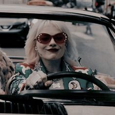 a woman with blonde hair and red glasses driving a car