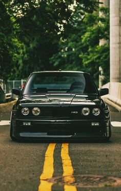 a black car parked on the side of a road next to a yellow line and trees