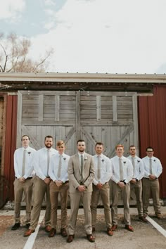 a group of men standing next to each other in front of a barn door with ties on