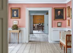 the hallway is painted pink and has portraits on the wall, along with two chairs