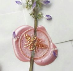 a pink wax stamp with a gold butterfly on it and flowers in the background,