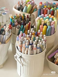 several buckets filled with markers and pens on a table next to other containers full of pens