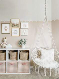 a white swing chair sitting next to a shelf with baskets on it and pictures above