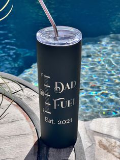 a black tumbler cup with a straw sticking out of it next to a swimming pool