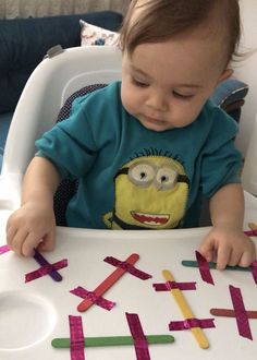 a toddler sitting in a highchair playing with colored stick letters that spell out the word x