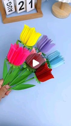 someone is holding up some colorful flowers in front of a blue table with calendars on it