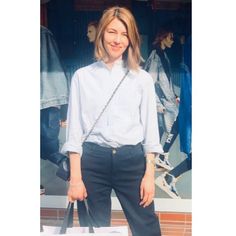 a woman standing in front of a store window holding a handbag and smiling at the camera