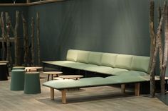 a green couch sitting next to two tables and stools on top of a wooden floor