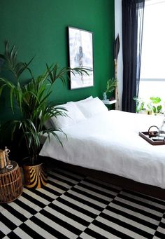 a bedroom with green walls and black and white striped rugs on the floor next to a bed