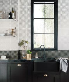 a black kitchen sink sitting under a window next to a shelf with bottles and glasses