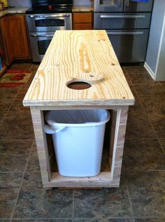 a kitchen island made out of wood with a trash can in the middle and a bucket on top