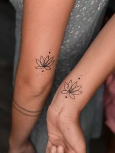 two women holding hands with matching tattoos on their arms, both showing the same flower