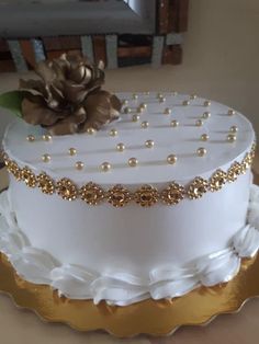 a white and gold decorated cake on a platter with a flower in the middle