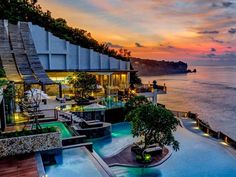 an outdoor swimming pool next to the ocean at sunset or sunrise with umbrellas and chairs