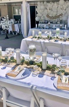 a table set up for an event with white balloons and greenery on the tables