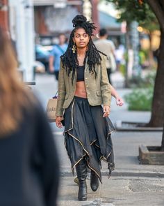 a woman with dreadlocks walking down the street wearing a skirt and jacket,