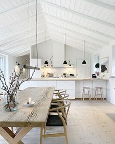 a wooden table sitting in the middle of a kitchen next to an island with stools