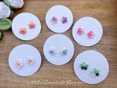 six little flower studs are sitting on a table next to some crocheted flowers