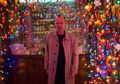 a man standing in front of a christmas tree with multicolored lights on it