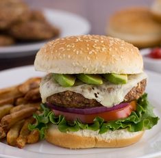 a hamburger with lettuce, tomato and onion on a plate next to french fries